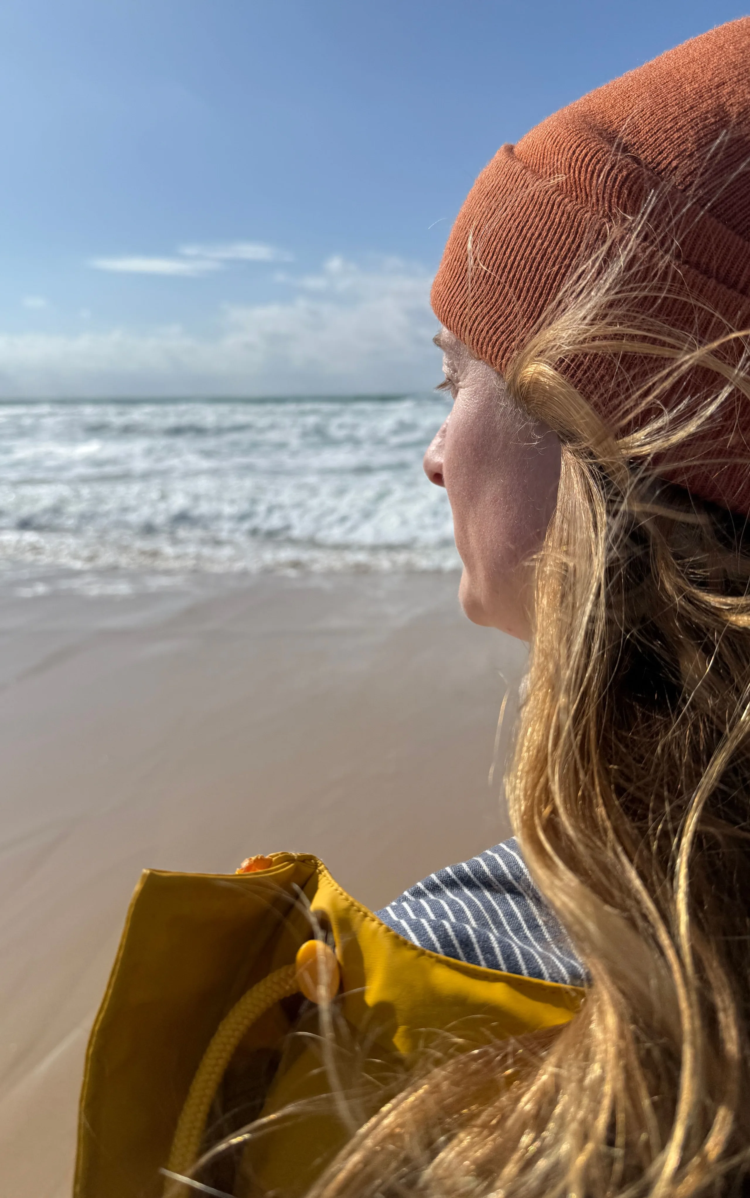 © Julia Federkiel Frau mit Mütze und gelbem Regenmantel blickt auf das Meer.